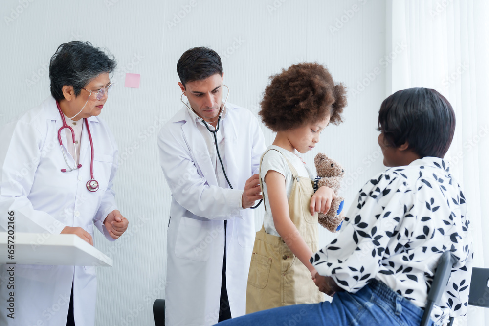Elderly woman doctor, male doctor, sitting asking about condition American girl, mother brought see doctor because daughter's abnormal symptoms, doctor got up examined girl's body before treating. Elderly woman doctor, male doctor, sitting asking about condition American girl, mother brought see doctor because daughter's abnormal symptoms, doctor got up examined girl's body before treating.
