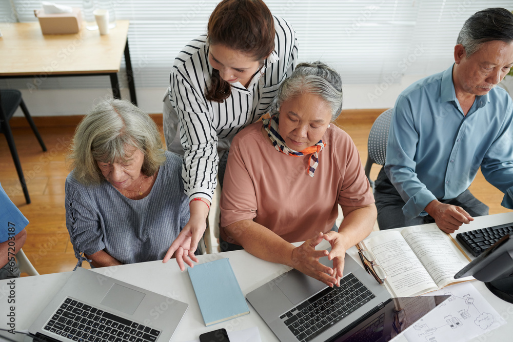Young woman helping confused elderly women to launch program on laptops Young woman helping confused elderly women to launch program on laptops