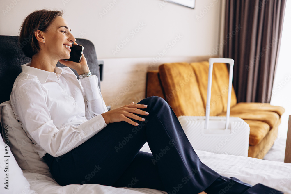 Business woman lying on a bed and talking on the phone in a hotel room Business woman lying on a bed and talking on the phone in a hotel room
