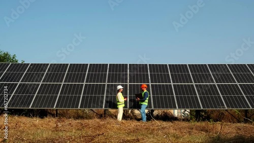 A man and a woman in hard hats and with a laptop are discussing work tasks against the backdrop of solar panels outside. Green electricity concept and making a deal photo
