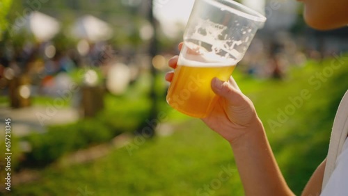 close up of beautiful happy young woman drinking beer and enjoying picnic at bravery beerpub backyard summer day. woman holding plastic glass with beer. party time outdoors.