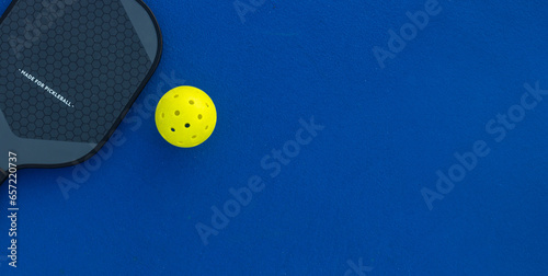 Pickleball tennis racket on the court. Blue background with copy space. Sport court and ball.