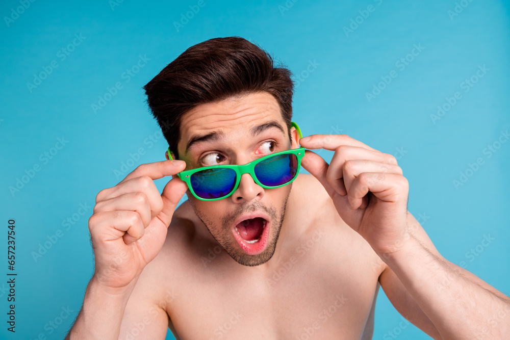 Photo portrait of nice young male astonished shock look empty space sunglass shirtless isolated on blue color background summer vacation
