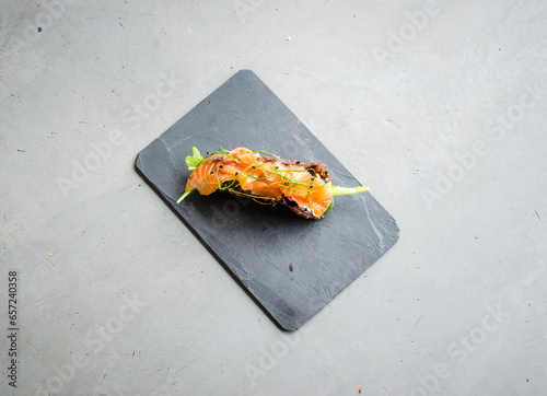 Smoked salmon elegantly served on a slice of toasted bread with fresh greens and herbs, arranged on a sleek black slate for a modern look