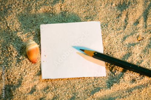 Background of shells in the sand with a piece of paper and a pencil