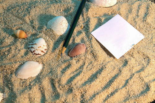 Background of shells in the sand with a piece of paper and a pencil