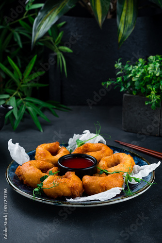 Crispy squid rings in dough with sauce and microgreens on a dark background.