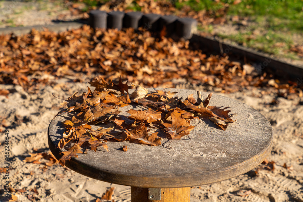 Round wooden table in the park strewn with yellow autumn leaves. Close up. Round wooden table in the park strewn with yellow autumn leaves. Close up.