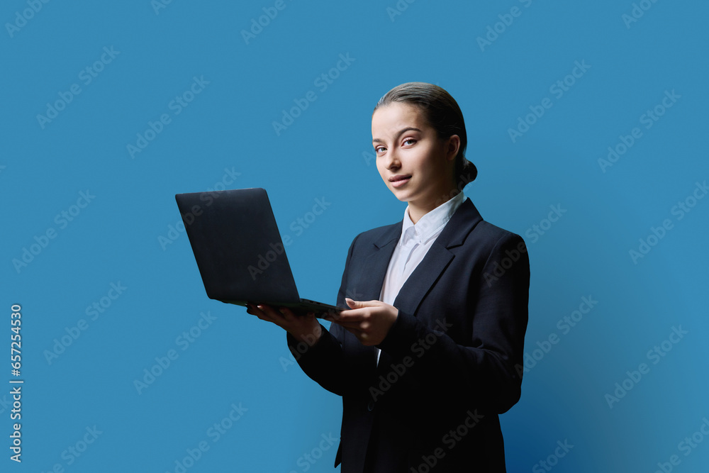 Teenage female student in formal style using computer laptop, on blue background