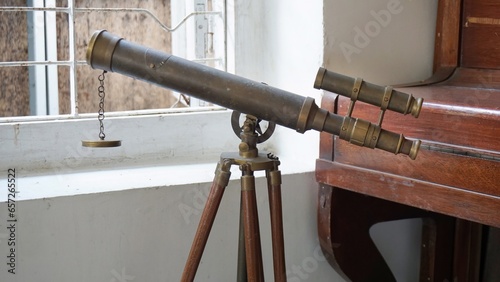 Old or antique telescope with old house and piano in the background