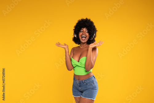 Energetic, happy, young woman with afro hairstyle dancing, laughing, listening music with wireless headphones