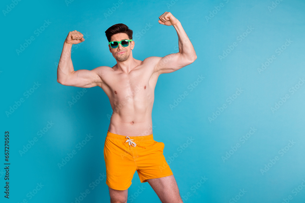 Photo portrait of handsome young guy raise fists flexing muscles wear trendy yellow shorts isolated on blue color background