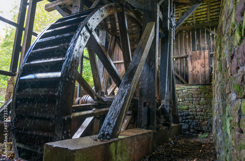 Giant colonial American hydro power wooden water wheel with mechanism and spokes visible inside stone machine house Hopewell Furnace Pennsylvania
