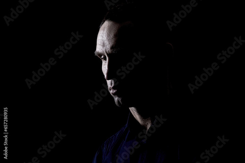 Portrait of a thoughtful man with chiaroscuro, a rocky and convex face, alone in the dark, with high contrast