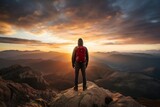 
A lone hiker stands atop a mountain at sunset
