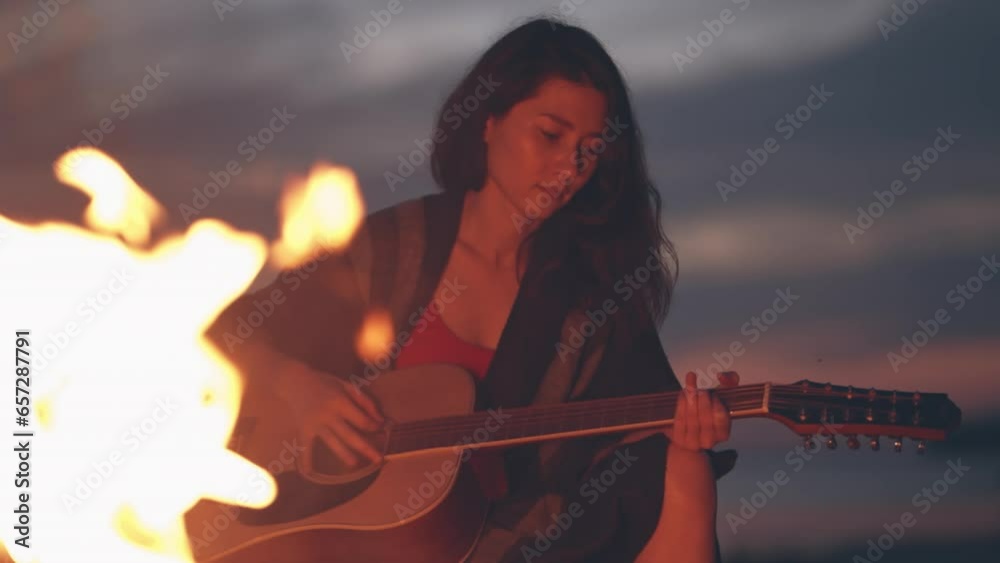 Lonely girl sitting by bonfire on the beach near forest playing acoustic guitar. Solo activity and social distancing.Spend free time in nature. Woman enjoying her loneliness. Summer vacation concept Lonely girl sitting by bonfire on the beach near forest playing acoustic guitar. Solo activity and social distancing.Spend free time in nature. Woman enjoying her loneliness. Summer vacation concept