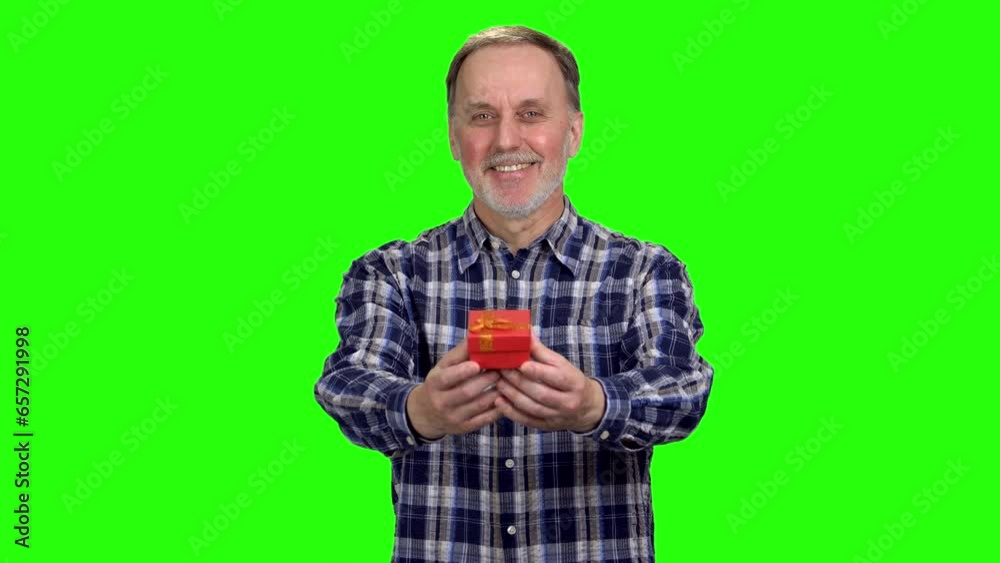 Smiling senior caucasian man gives you a small gift box. Isolated on green. Smiling senior caucasian man gives you a small gift box. Isolated on green.