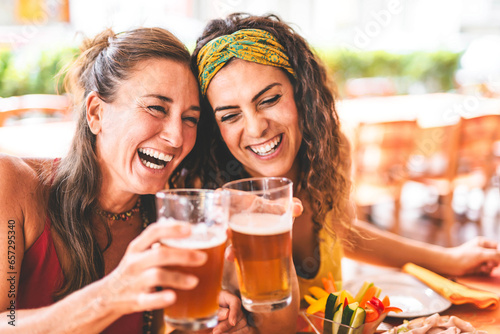 Happy women having fun drinking beer outdoors at pub terrace  Two girls friends toasting glass of pint at brewery pub enjoying food  Social Lifestyle concept with happy young people