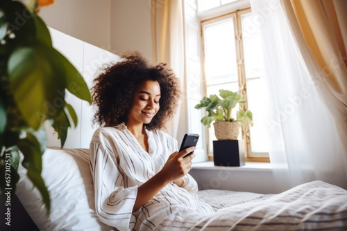 Beautiful smiling black woman laying in bed and scrolling on her phone at home