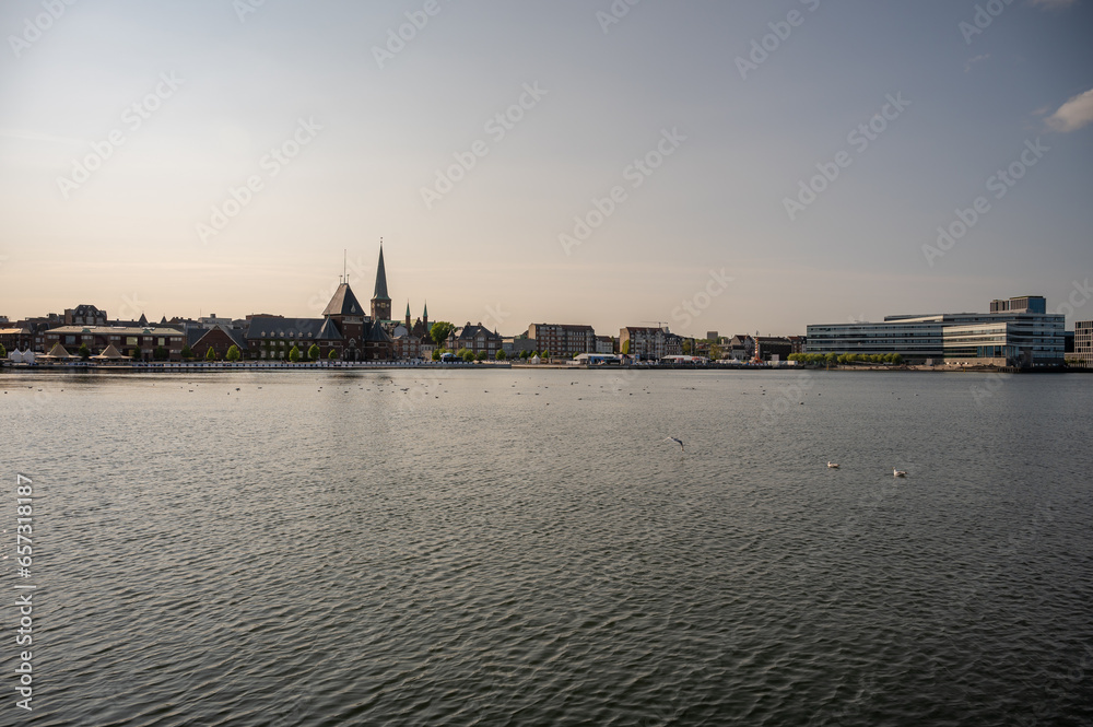 Cityscape of Aarhus Denmark in the evening with cathedral of Aarhus, seagulls on the sea in front, wide angle shot, sunset mood