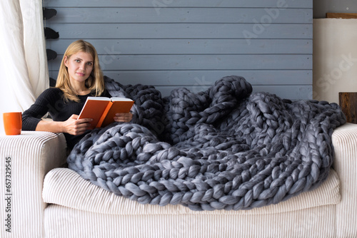 A woman in a black sweater is lying down reading a book, wrapped in a beautiful gray merino blanket.