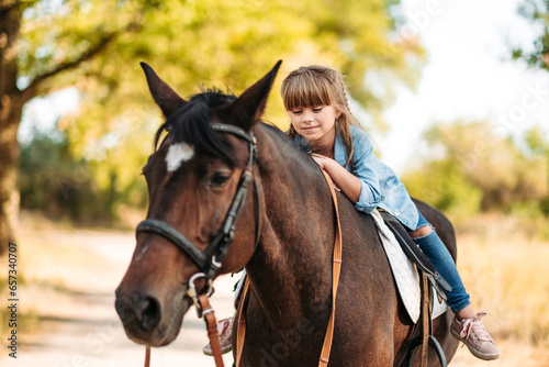 Cute little girl with long hair riding a horse outdoors. Pet therapy