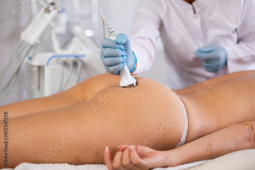 Fotografie Aesthetician administering hardware procedure on buttocks of young female patien
