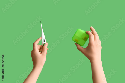 Doctor with thermometer and pill box on green background