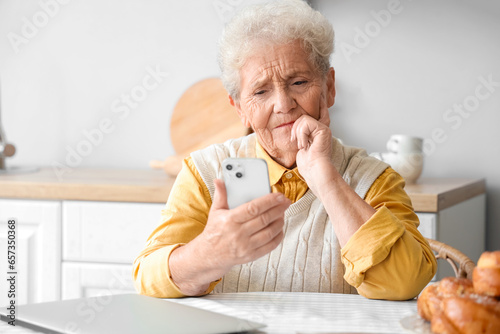 Thoughtful senior woman using mobile phone in kitchen