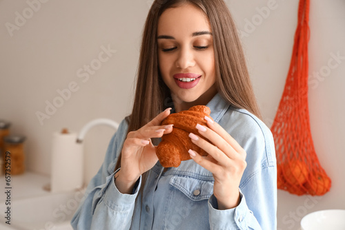 Beautiful young woman with tasty croissant in kitchen