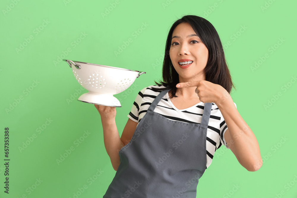 Happy beautiful Asian woman pointing at colander on green background Happy beautiful Asian woman pointing at colander on green background