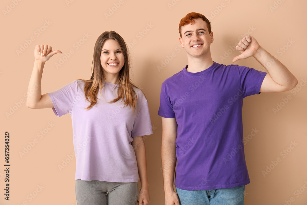 Young couple pointing at their t-shirts on beige background Young couple pointing at their t-shirts on beige background