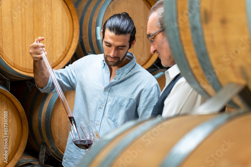 Group of Man and woman sommelier tasting red wine in wooden barrel at vintage wine cellar at wine factory. Winery, wine shop, brewery liquor business manufacturing industry and winemaker concept.