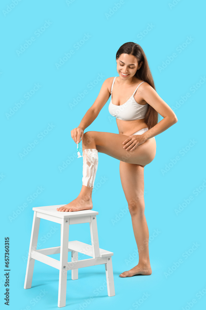 Beautiful young woman shaving legs on blue background