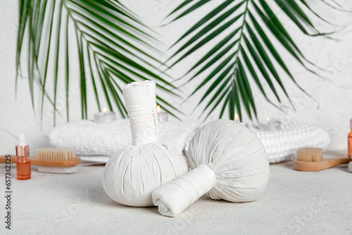 Massage herbal bags, spa accessories and palm leaves on light background
