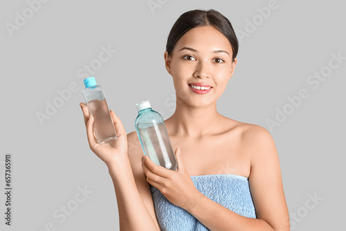 Young Asian woman with bottles of micellar water on light background