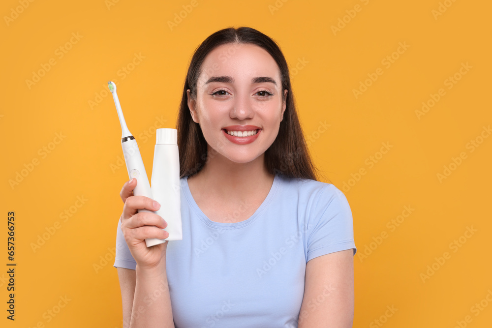 Happy young woman holding electric toothbrush and tube of toothpaste on yellow background Happy young woman holding electric toothbrush and tube of toothpaste on yellow background