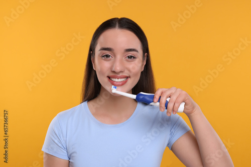 Happy young woman holding electric toothbrush on yellow background