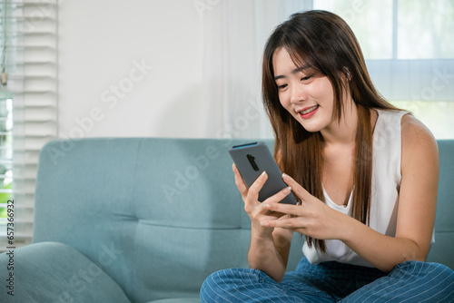 Social media networks. Happy beautiful female relax and shopping online with smartphone, Smiling Asian woman sitting on sofa reading news on mobile smart phone at living room at home