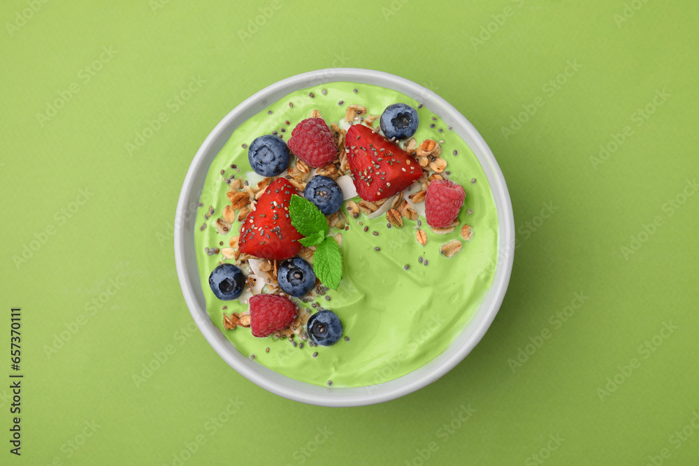 Tasty matcha smoothie bowl served with berries and oatmeal on green background, top view. Healthy breakfast