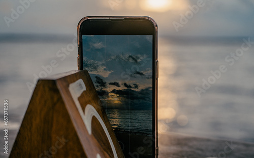 hermoso cuadro donde se ve un telefono celular tomando una foto a un atardecer increible en la playa photo