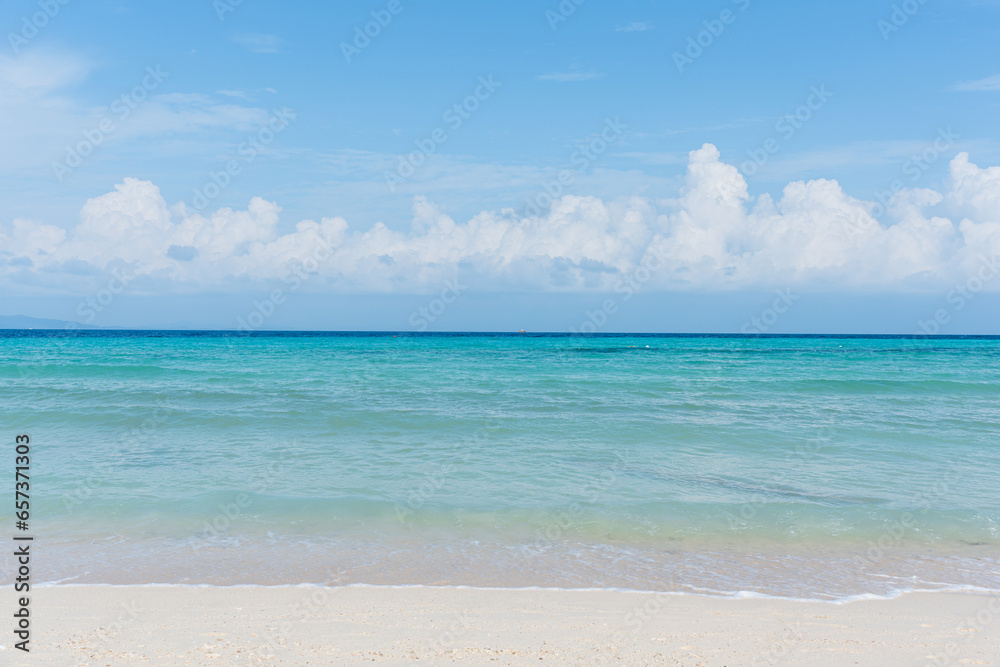 Sandy beach with rolling calm wave of ocean on sunny day on background white clouds in blue sky