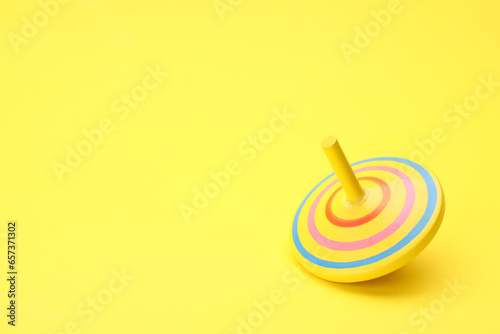 One bright spinning top on yellow background, space for text. Toy whirligig photo