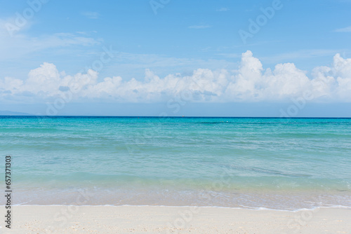 Sandy beach with rolling calm wave of ocean on sunny day on background white clouds in blue sky