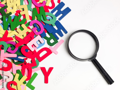 Learning and education concept. Scattered colorful alphabet with a magnifying glass against white background.
