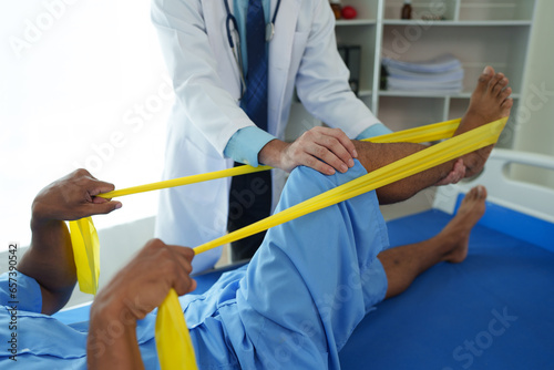 Physical therapist gives resistance band therapy to the legs and knees of an athletic male patient. Physical therapy concept
