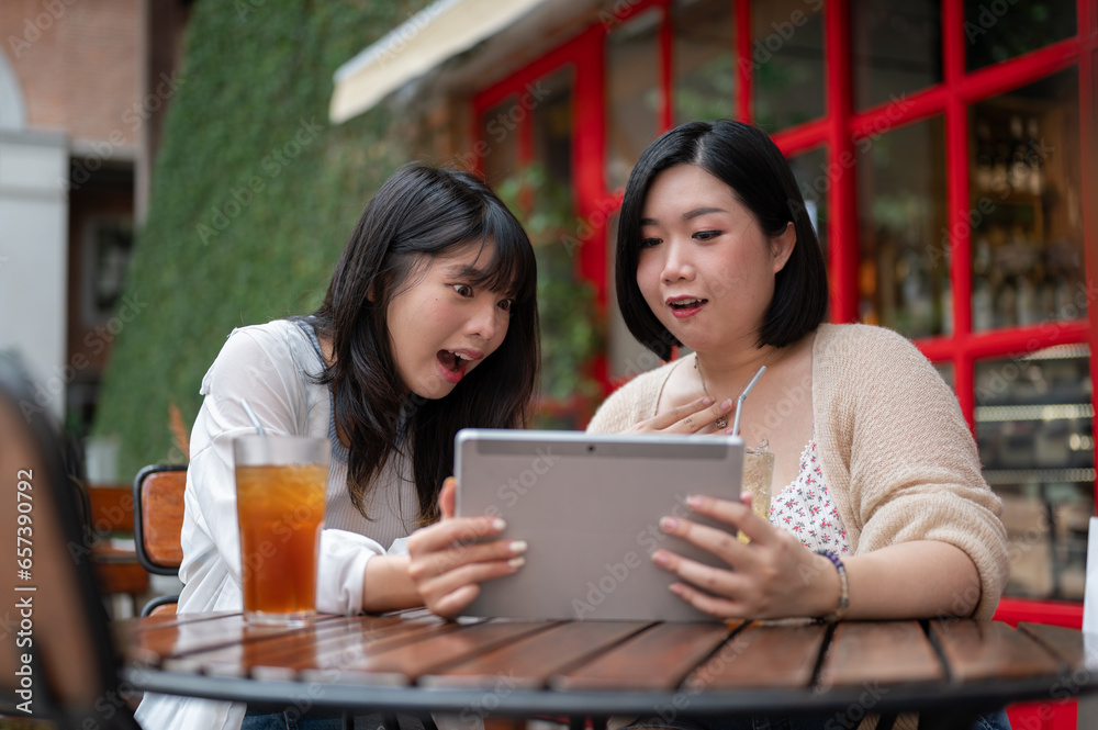 Two surprised Asian female friends are watching an interesting video on a tablet together. Two surprised Asian female friends are watching an interesting video on a tablet together.