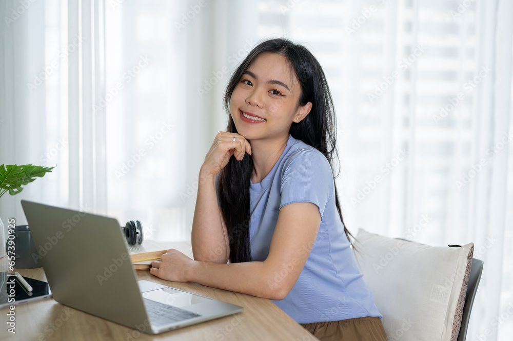 An attractive Asian woman sitting at a table in her home office and smiling at the camera. An attractive Asian woman sitting at a table in her home office and smiling at the camera.