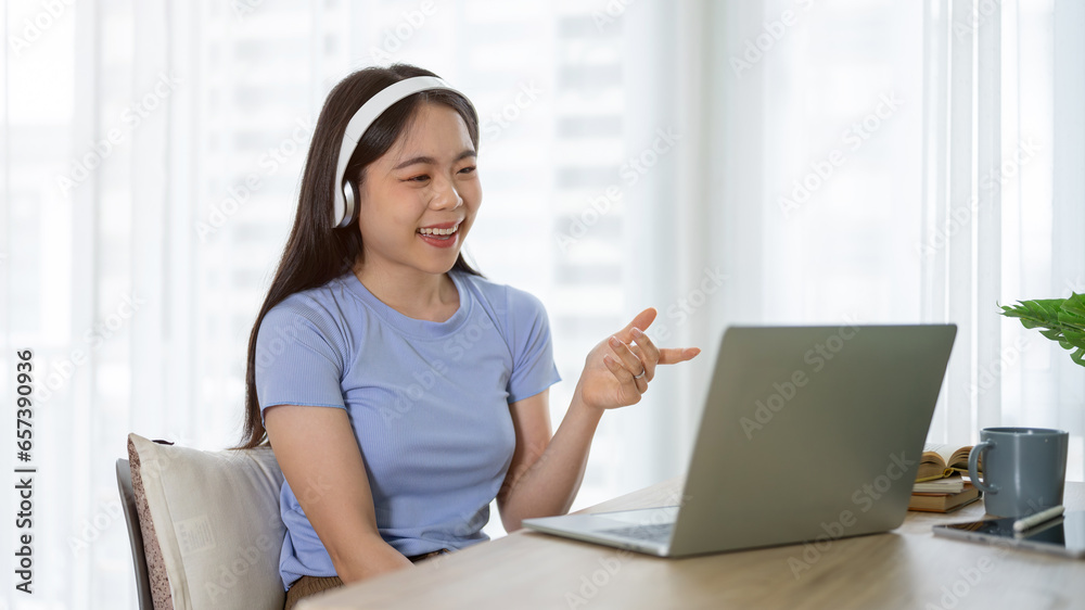 Naklejka premium A cheerful Asian woman in headphones is talking on an online meeting or online job interview.