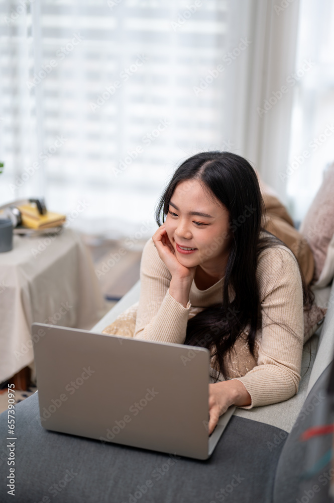 A beautiful Asian woman is using her laptop, watching a movie while lying on a sofa. A beautiful Asian woman is using her laptop, watching a movie while lying on a sofa.